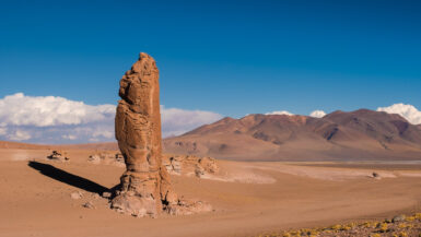 High pillar brown rock in the middle of the desert of altiplano surrounded by high Volcanos