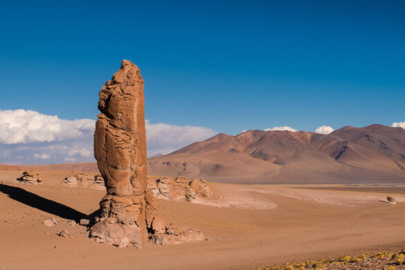 High pillar brown rock in the middle of the desert of altiplano surrounded by high Volcanos