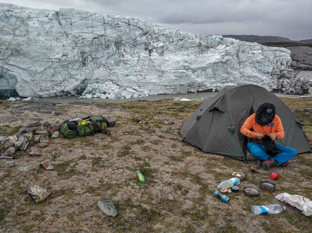 Man camping in his tent on the ground infront of the Greenland ice-cap edge.