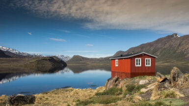 Red hut in Greenland near the lake with mountains in background