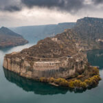 a castle carved in the rock wall with a Tigris river around it