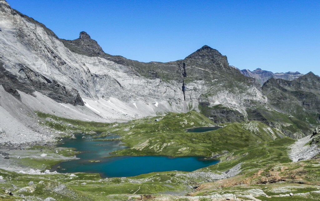 Magnificient high rocky mountains rising above mountain lake surrounded by green grass in a good weather