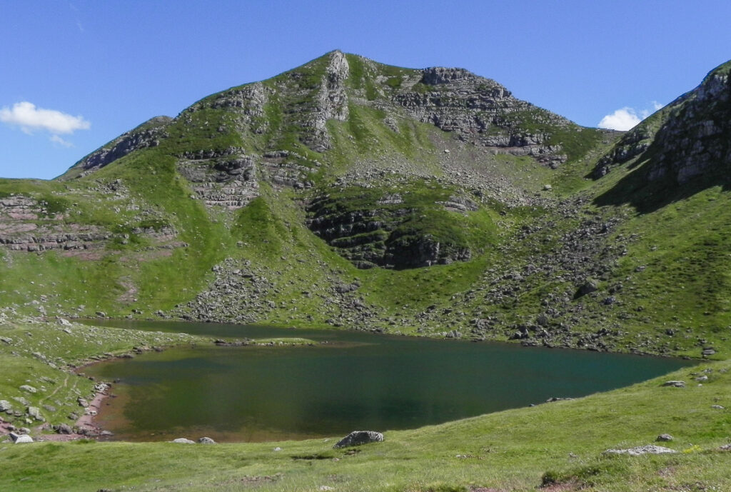 small mountain lake just above the high green grassy mountain in the calm weather in summer