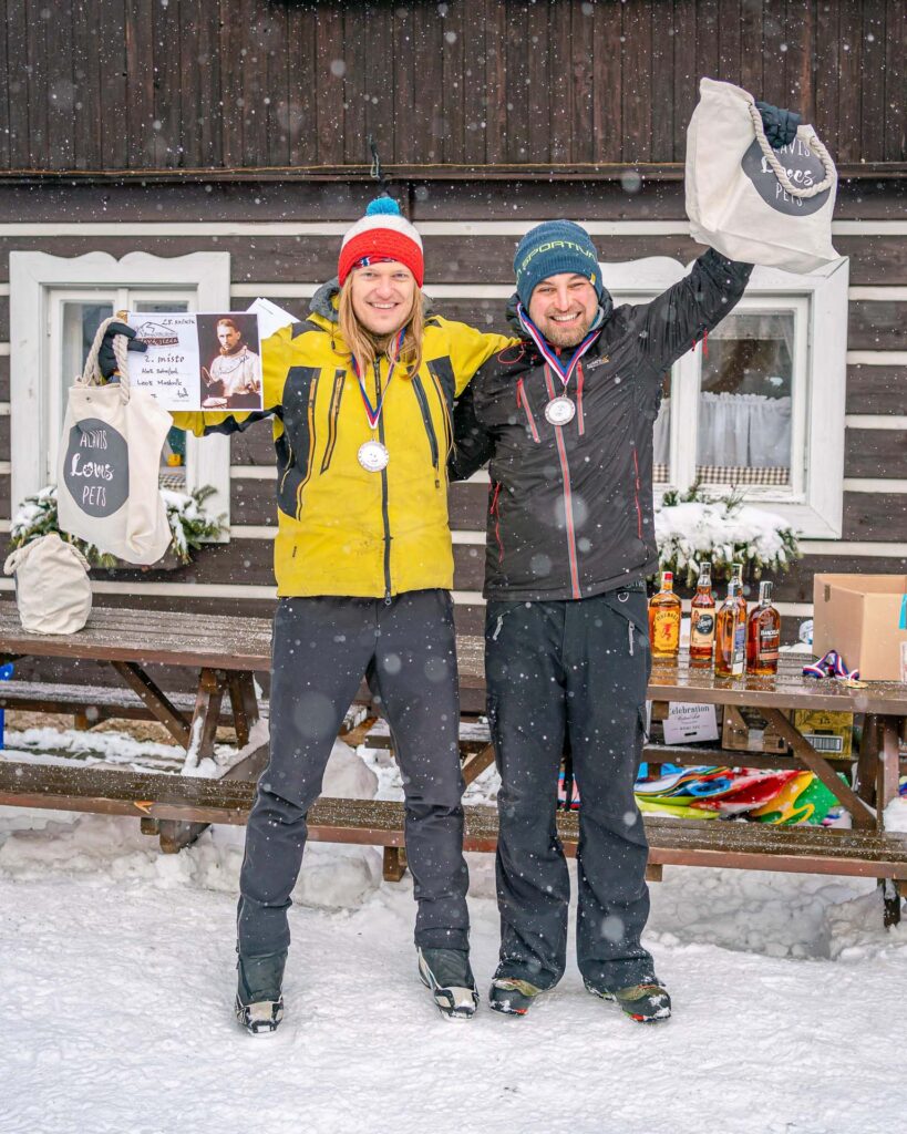 two guys with their race medals infront of the wooden house