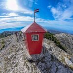 Red metal shelter on top of DInara Mountain with a Croatian flag on top