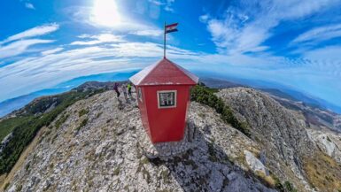 Red metal shelter on top of DInara Mountain with a Croatian flag on top