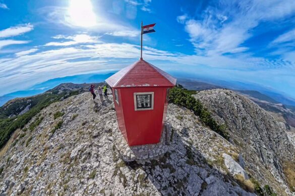 Red metal shelter on top of DInara Mountain with a Croatian flag on top