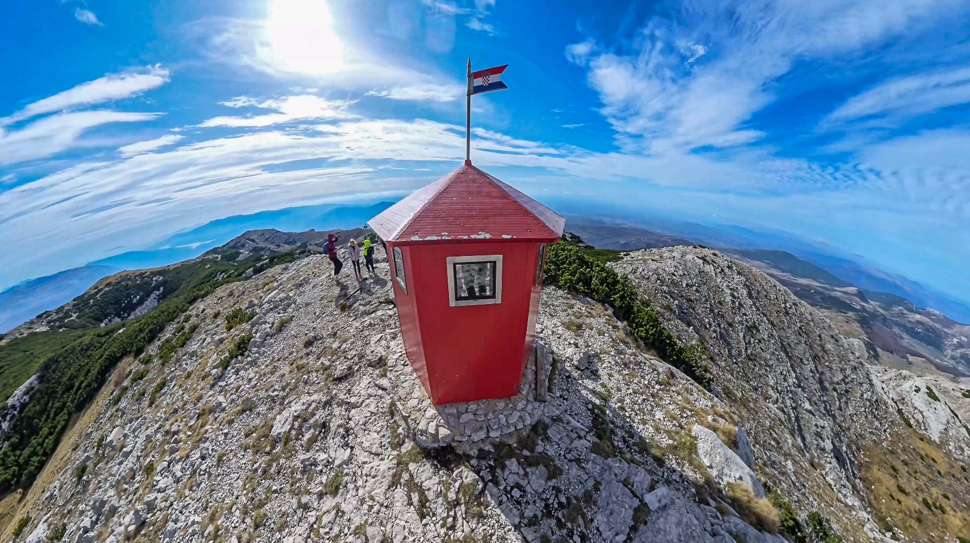 Red metal shelter on top of DInara Mountain with a Croatian flag on top