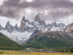 sharp spiky mountains above the yellow pampa and glacier below surrounded by brown clouds