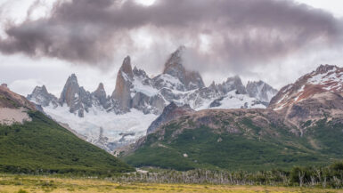 sharp spiky mountains above the yellow pampa and glacier below surrounded by brown clouds