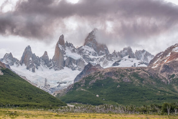 sharp spiky mountains above the yellow pampa and glacier below surrounded by brown clouds