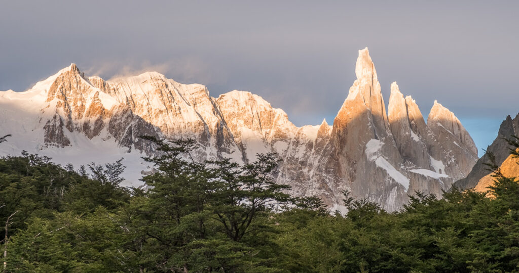 Sharp spike like monolith rising over the high ridge and rorrests lighted by the sunrise