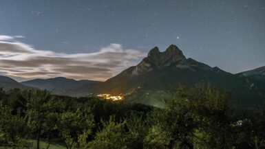 Sharp pitchfork stone moholith standing high iat night with the small village below