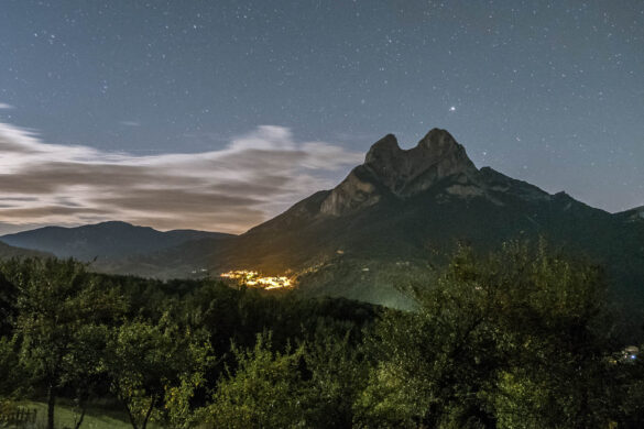 Sharp pitchfork stone moholith standing high iat night with the small village below