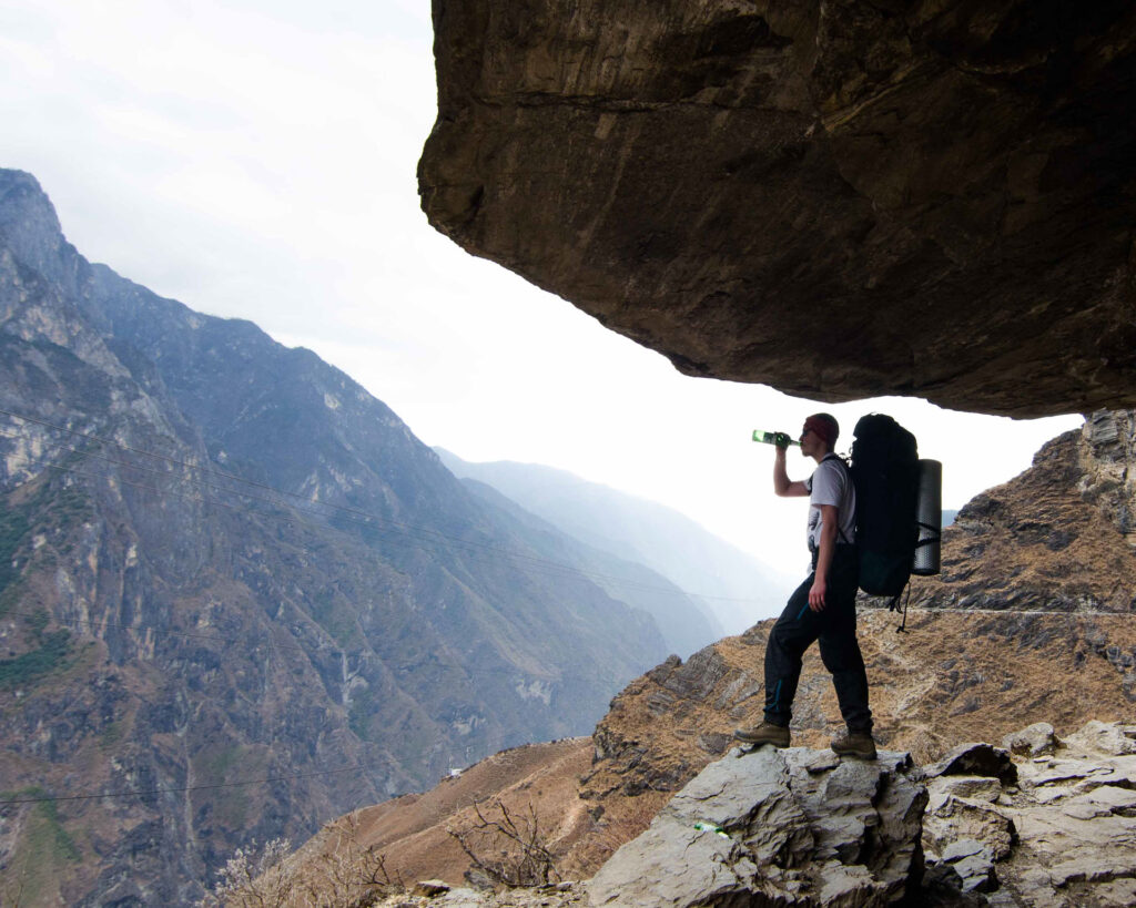 Guy drinking a beer in the high mountains under the overhanging rock