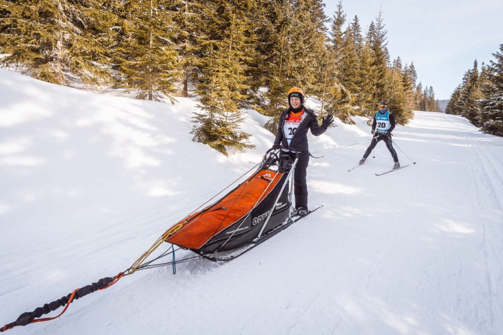 Musher girl on a sled with a skier behind on Ledová Jízda race